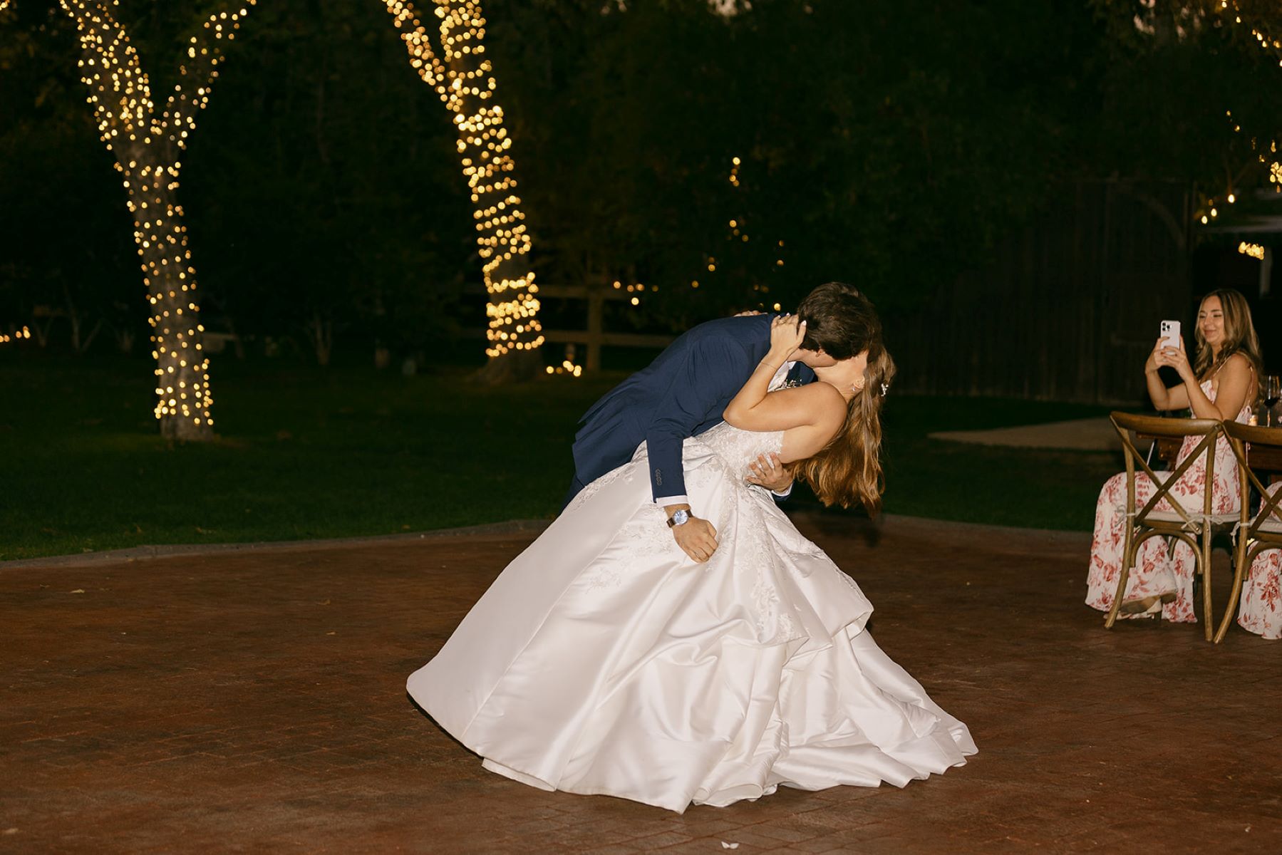 A couple at their wedding reception the groom is dipping the bride and kissing her the bride is wearing a white wedding dress and the groom is wearing a tuxedo