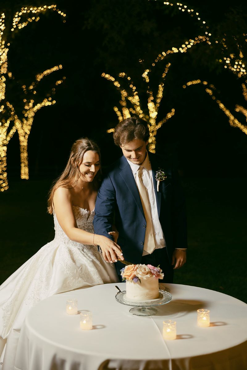 A couple at their reception cutting their wedding cake together the bride is wearing a white wedding dress the groom is wearing a tuxedo 