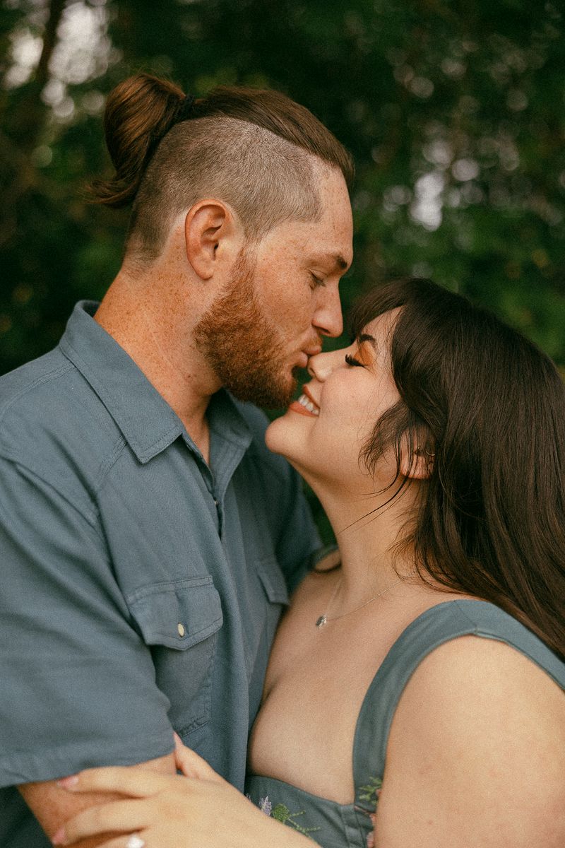 a man kissing his partner's nos and the woman is smiling with her eyes closed