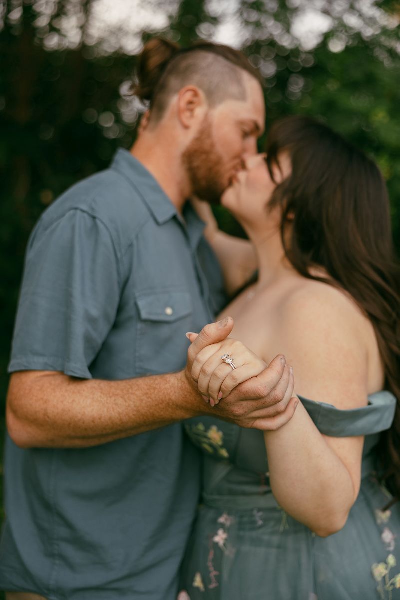 a man and woman kissing and holding up their hands the woman is wearing her engagement ring 