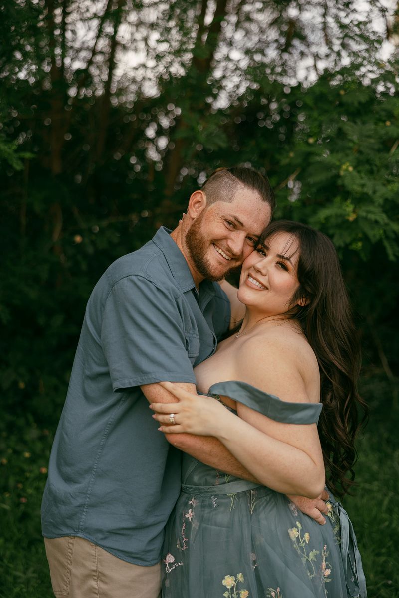 a man and woman hugging and msiling the woman is wearing a blue dress with flowers the man is wearing a blue button up 