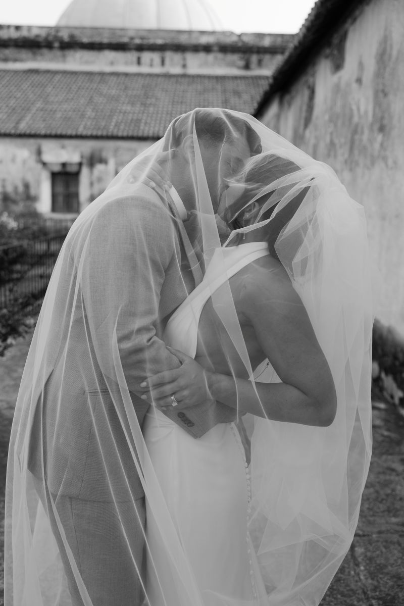 a couple kissing underneath the bride's veil and embracing