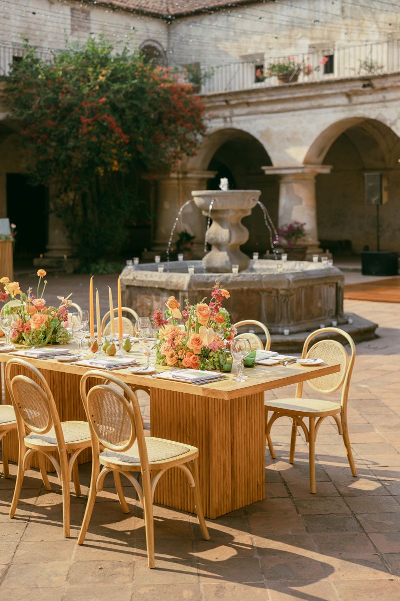 a fountain next to it is a long banquet table elegantly decorated with candles, flowers, plates, and glasses