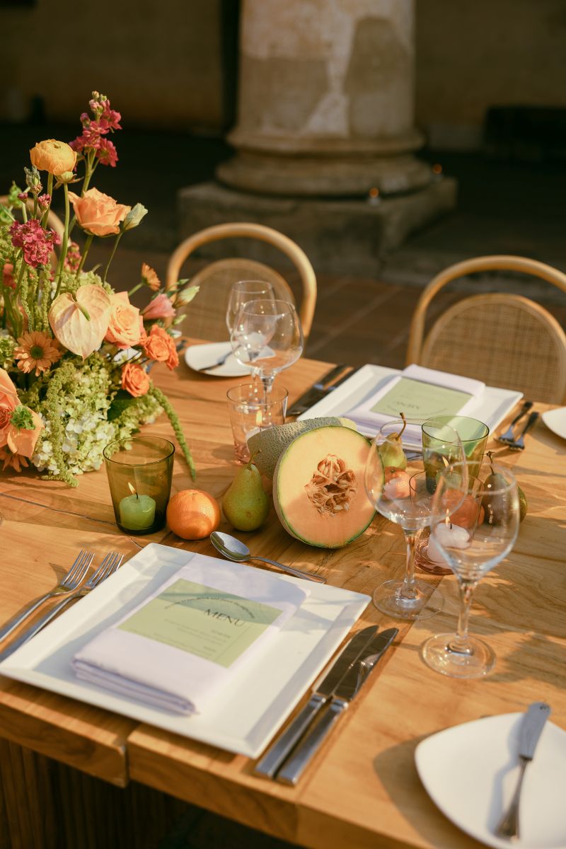 a wooden banquet tables decorated with flowers, fruits, glasses, plates and candles