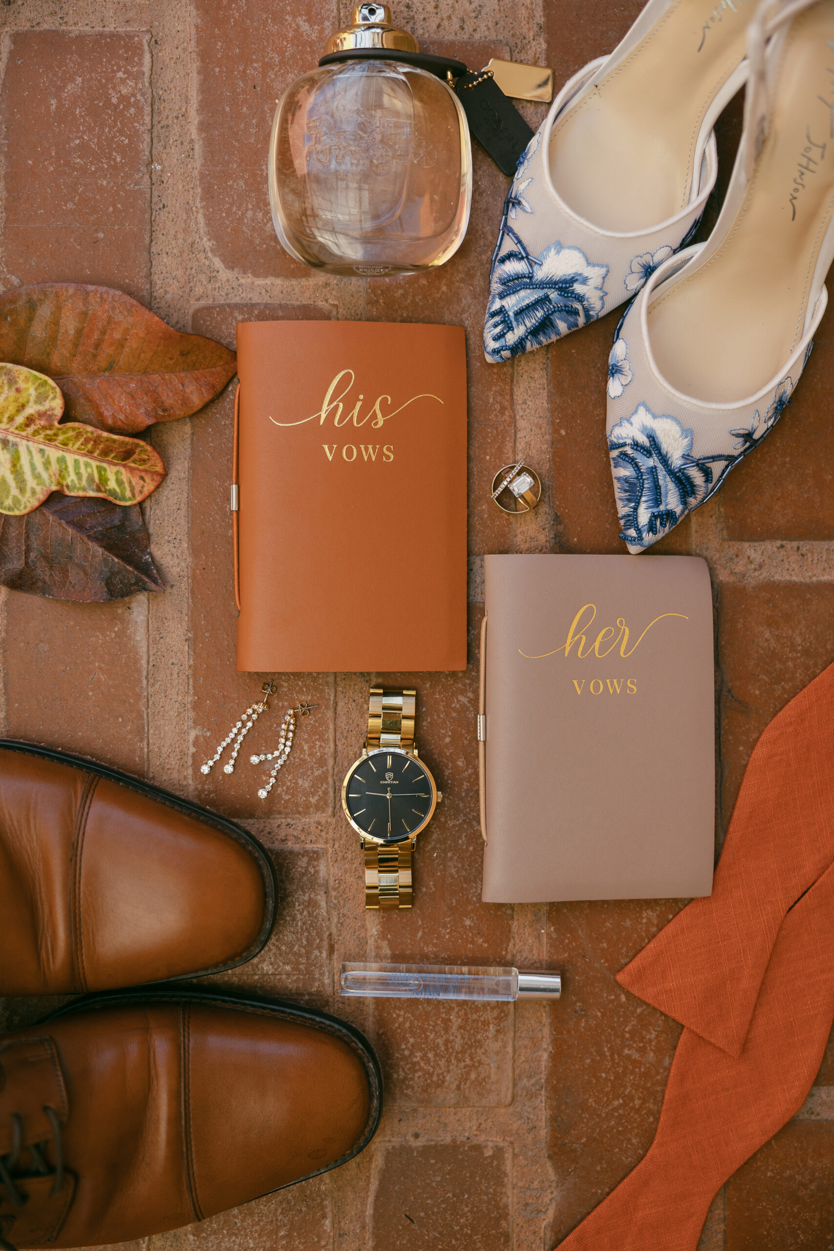 a flat lay of wedding details including vow books, whoes, watches, and jewelery